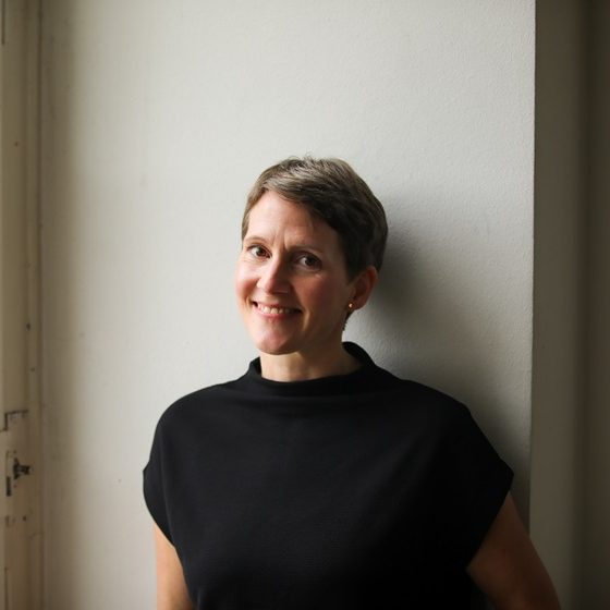 Portraitfoto Ina Hartmann, Texterin Portraitfoto von Ina Hartmann, Texterin und Autorin. Sie hat kurze Haare und ein offenes Lächeln, trägt ein schwarzes Shirt.